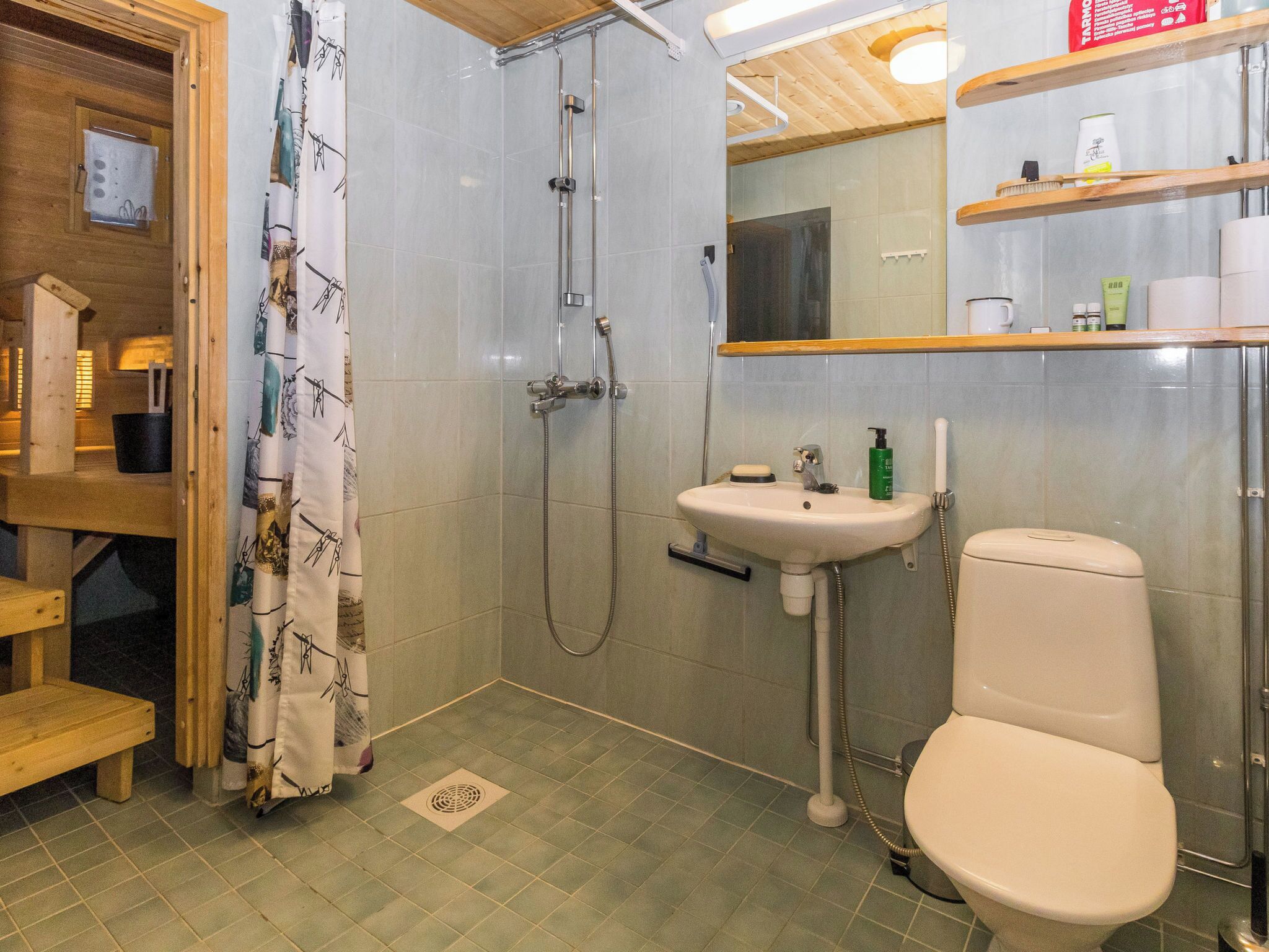 A bathroom with a shower, sink, toilet, and wooden shelves with toiletries.