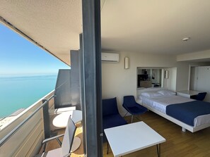 A balcony with a view of the sea, a bed, a desk, and a chair. - Orbi City Apartaments  (Batumi)