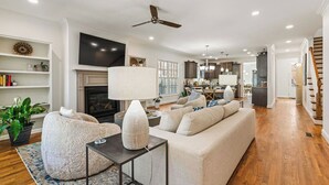 A spacious living room with a fireplace, a large sofa, a coffee table, and a television. - New! Fig Tree House! Near Downtown, Hot Tub, 3 Kings, Pets/Family/Work Friendly (Greenville)