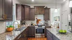 A modern kitchen with dark wood cabinets, stainless steel appliances, granite countertops, and a wooden floor. - New! Fig Tree House! Near Downtown, Hot Tub, 3 Kings, Pets/Family/Work Friendly (Greenville)