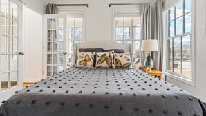 A bedroom with a large bed, two windows, and a nightstand with a lamp. - New! Fig Tree House! Near Downtown, Hot Tub, 3 Kings, Pets/Family/Work Friendly (Greenville)