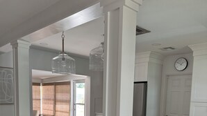Een moderne keuken met een centraal eiland, barkrukken, hanglampen en een klok aan de muur.