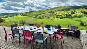 Un espace de restauration en plein air, avec des tables et des chaises, offrant une vue sur un paysage verdoyant composé de collines et d’arbres.