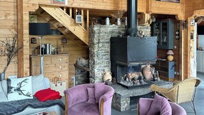 Un intérieur chaleureux avec des éléments en bois, une cheminée en pierre, des fauteuils violets et un escalier en bois.