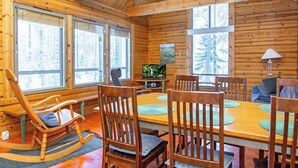 Interno di una baita in legno con un tavolo da pranzo, sedie, una poltrona a dondolo e un televisore.