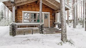 Una baita di legno con facciata in legno, un portico anteriore e una finestra che si affaccia su una foresta innevata.