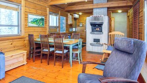 Interno di una baita in legno con zona pranzo, camino e una grande finestra.