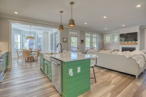 A spacious kitchen with a large island, a dining area with chairs, and a living area with a sofa and fireplace. - NEW! 10 min. Walk to Town & Beach, PVT Hot Tub + Fenced Yard, Bikes, Fire-pit (Pacific Beach)