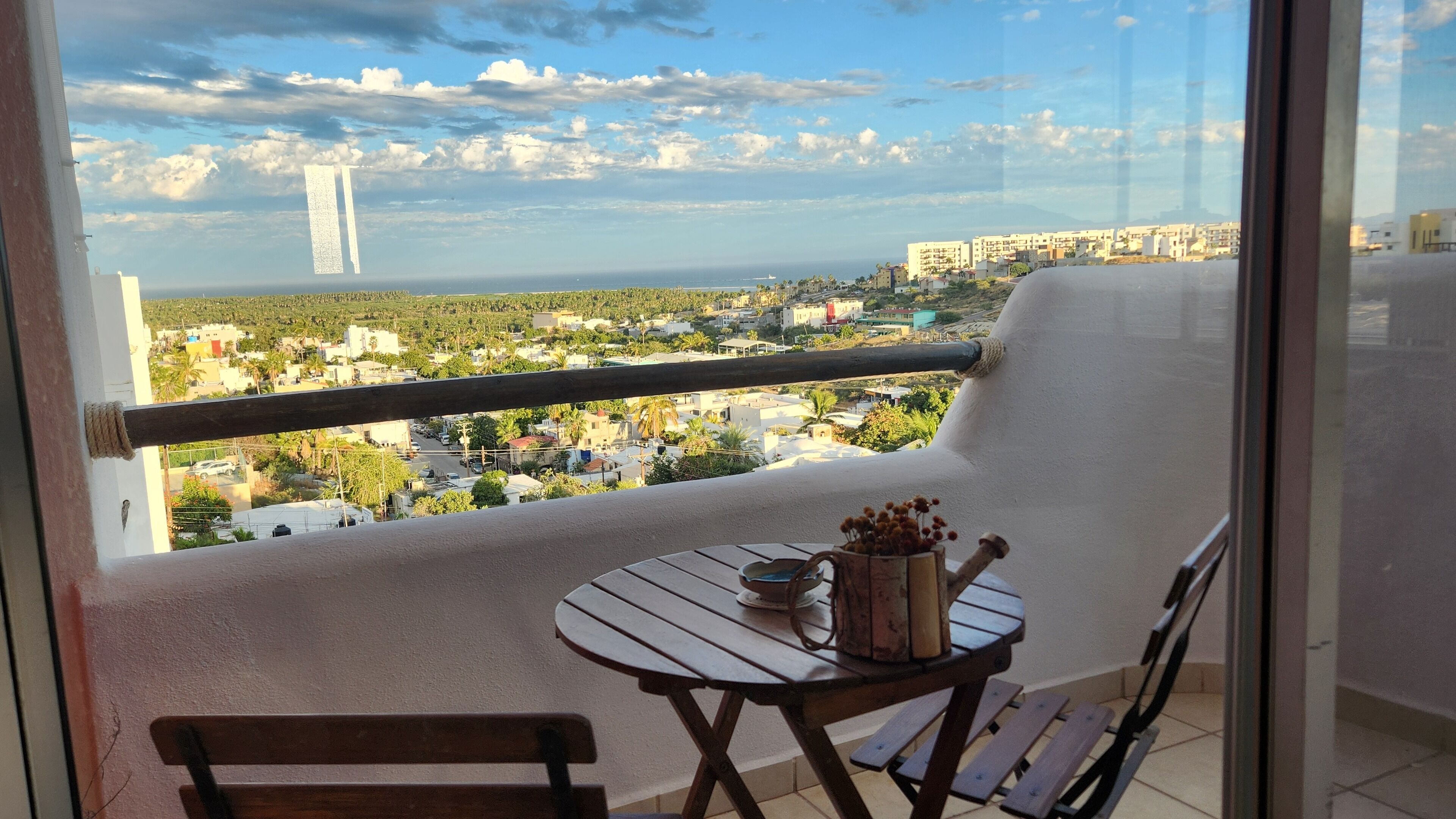 Uma varanda com vista para a paisagem urbana costeira, uma mesa com um vaso e uma cadeira.