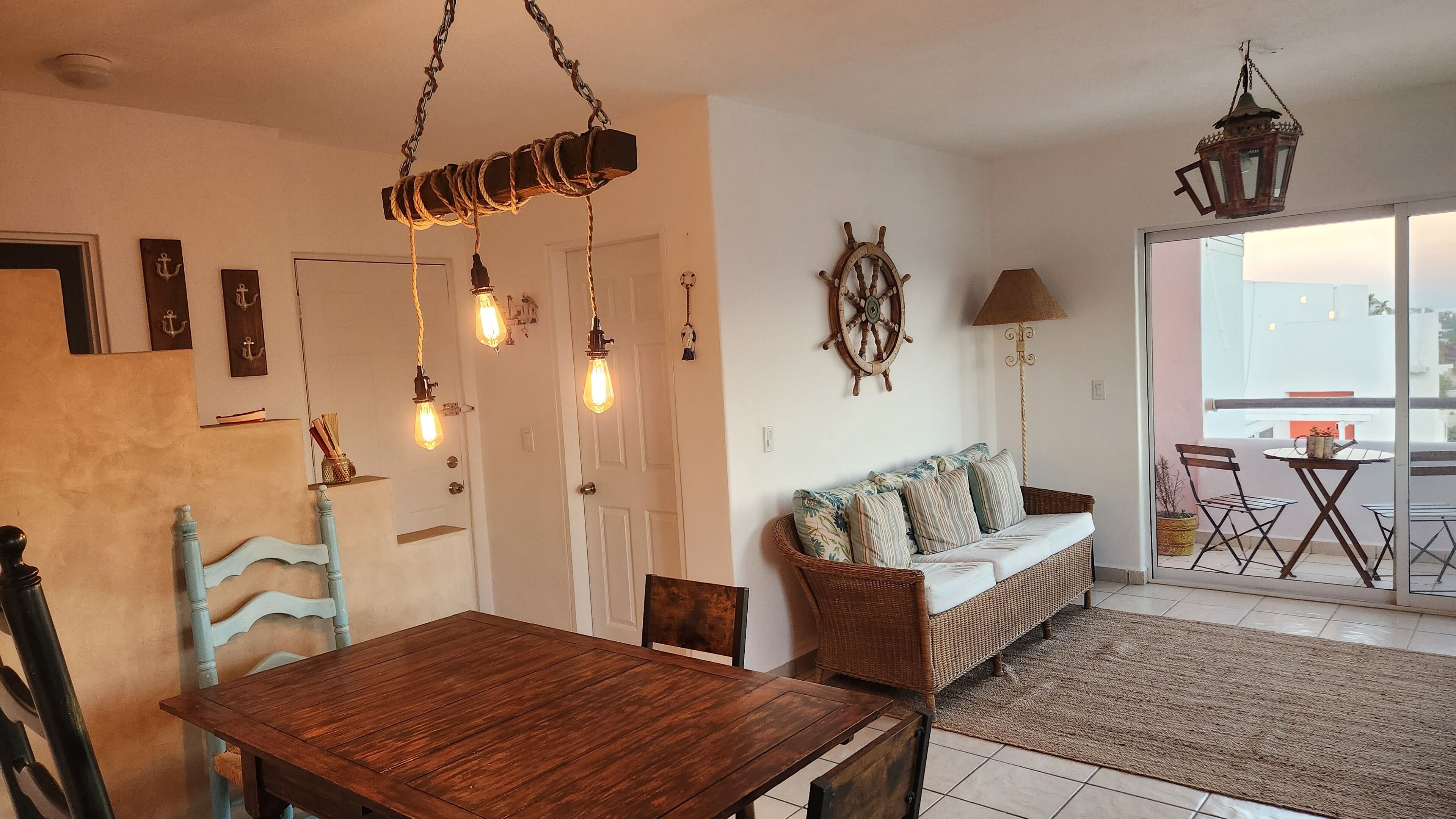 Un coin repas avec une table et des chaises en bois, un canapé en osier et une vue sur l’extérieur grâce à une porte-fenêtre coulissante.