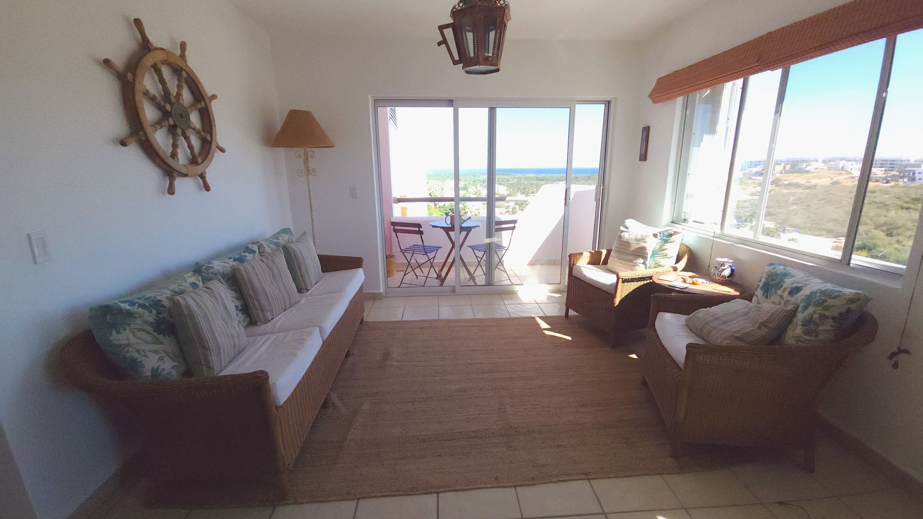 A living room with a sofa, two armchairs, a table, and a view through a glass door to an outdoor balcony.