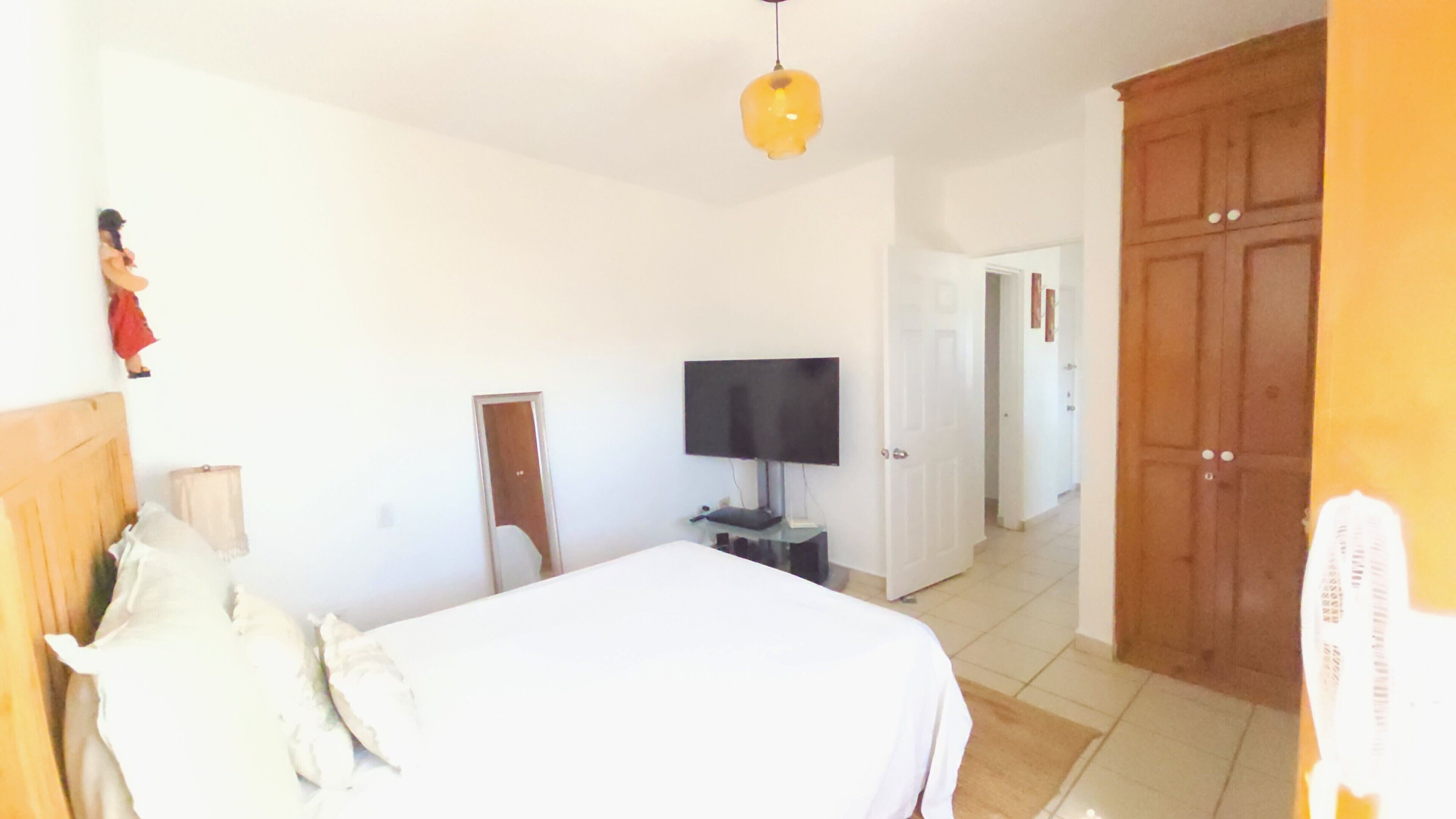 Une chambre à coucher avec un lit, un téléviseur posé sur un meuble, une armoire et une porte donnant sur une autre pièce.