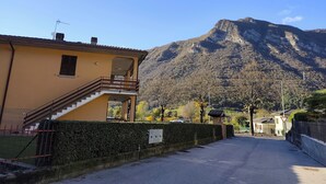 Un edificio con balcón y escalera, un camino que lleva a una montaña, y un cielo despejado.