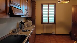Una cocina con armarios de madera, estufa empotrada, ventana con persianas e iluminación colgante.