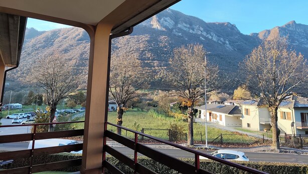 Vista desde un balcón con montañas al fondo, un estacionamiento y edificios residenciales.