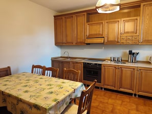 A kitchen with wooden cabinets, a dining table with a floral tablecloth, and a sink. - House at the Lake-a stone's throw from the beach (Crone)