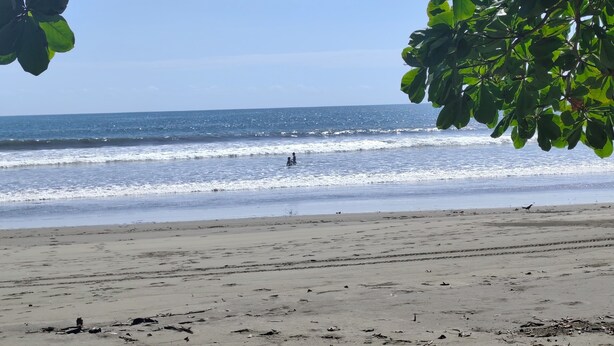 A beach with waves, a clear sky, and a person in the water. - Apartment with access to the beach, a place to stroll beautiful experience. (Quepos)