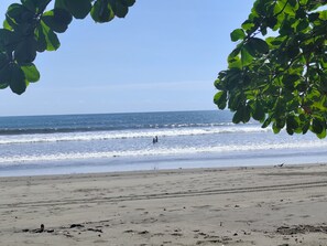 Uma praia com ondas, céu claro e uma pessoa na água.