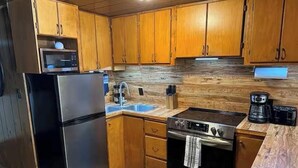 A kitchen with wooden cabinets, a stainless steel refrigerator, a microwave, a sink, a stove, and a coffee maker. - Winterfell Mountain Retreat (Island Park)