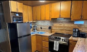 A kitchen with wooden cabinets, a stainless steel refrigerator, a microwave, a sink, a stove, and a coffee maker.