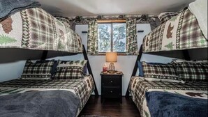 A room with two beds, each with a patterned blanket and matching pillows. There is a small table with a lamp in the center. - Winterfell Mountain Retreat (Island Park)