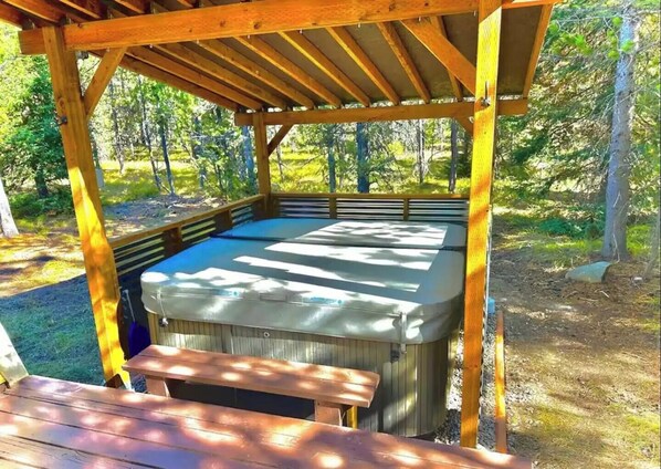 A hot tub under a wooden pergola in a wooded area.