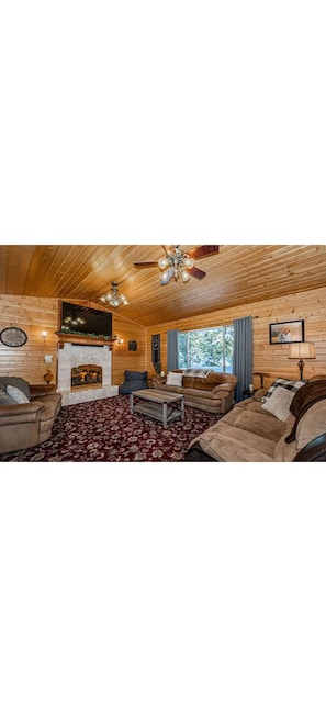 A cozy log cabin interior with a fireplace, wooden ceiling, and plush furniture.