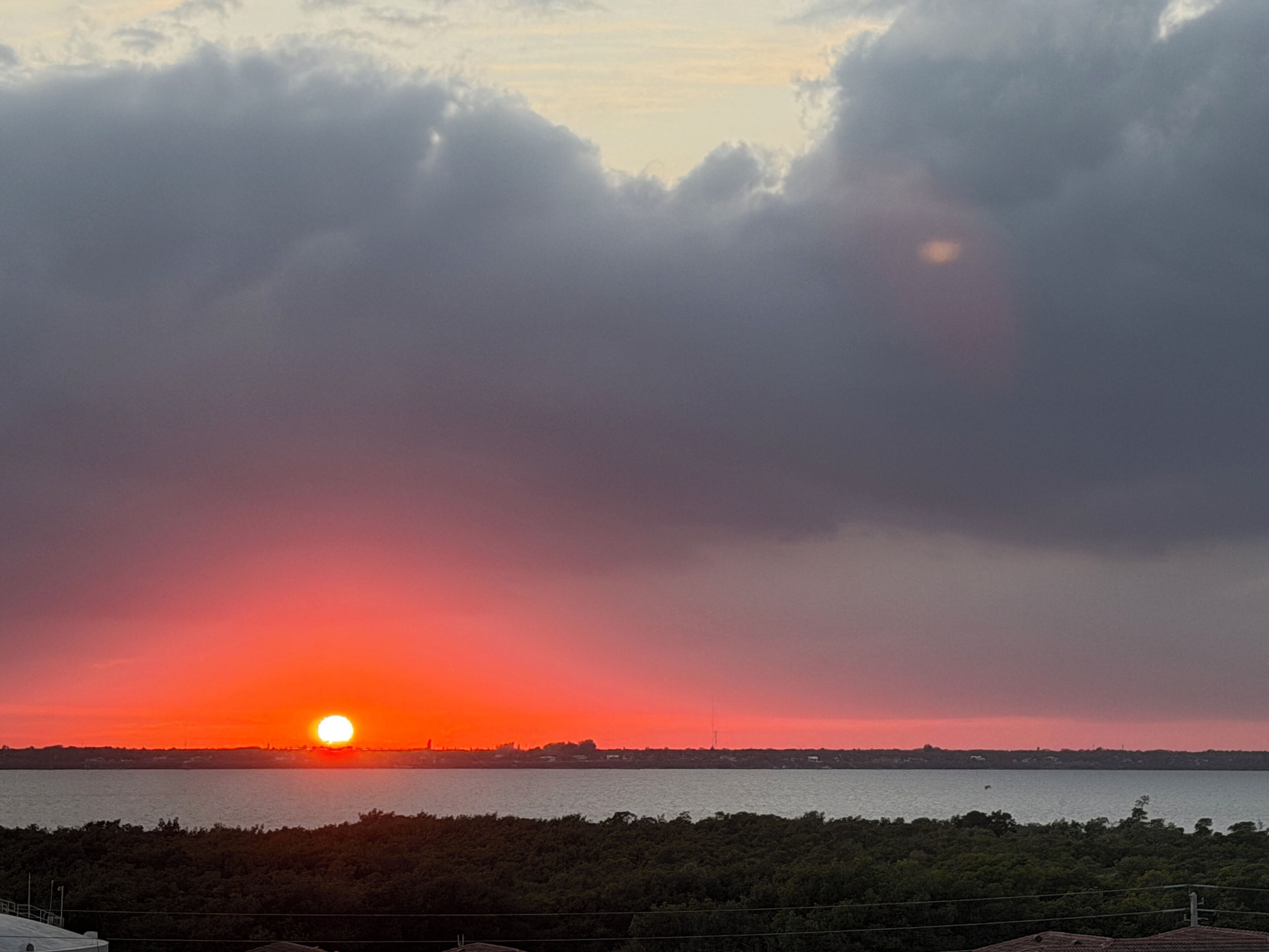 A sunset over a body of water with a silhouette of a city skyline in the distance.
