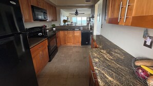 A kitchen with wooden cabinets, a black refrigerator, a microwave, and a granite countertop. - ENJOY SUNRISES, SUNSETS FROM THIS BEAUTIFUL 7TH FLOOR HUTCHINSON ISLAND CONDO!! (Jensen Beach)