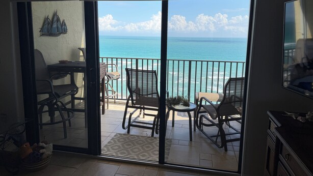 A room with a sliding glass door leading to a balcony with ocean views, furnished with chairs and a table. - ENJOY SUNRISES, SUNSETS FROM THIS BEAUTIFUL 7TH FLOOR HUTCHINSON ISLAND CONDO!! (Jensen Beach)