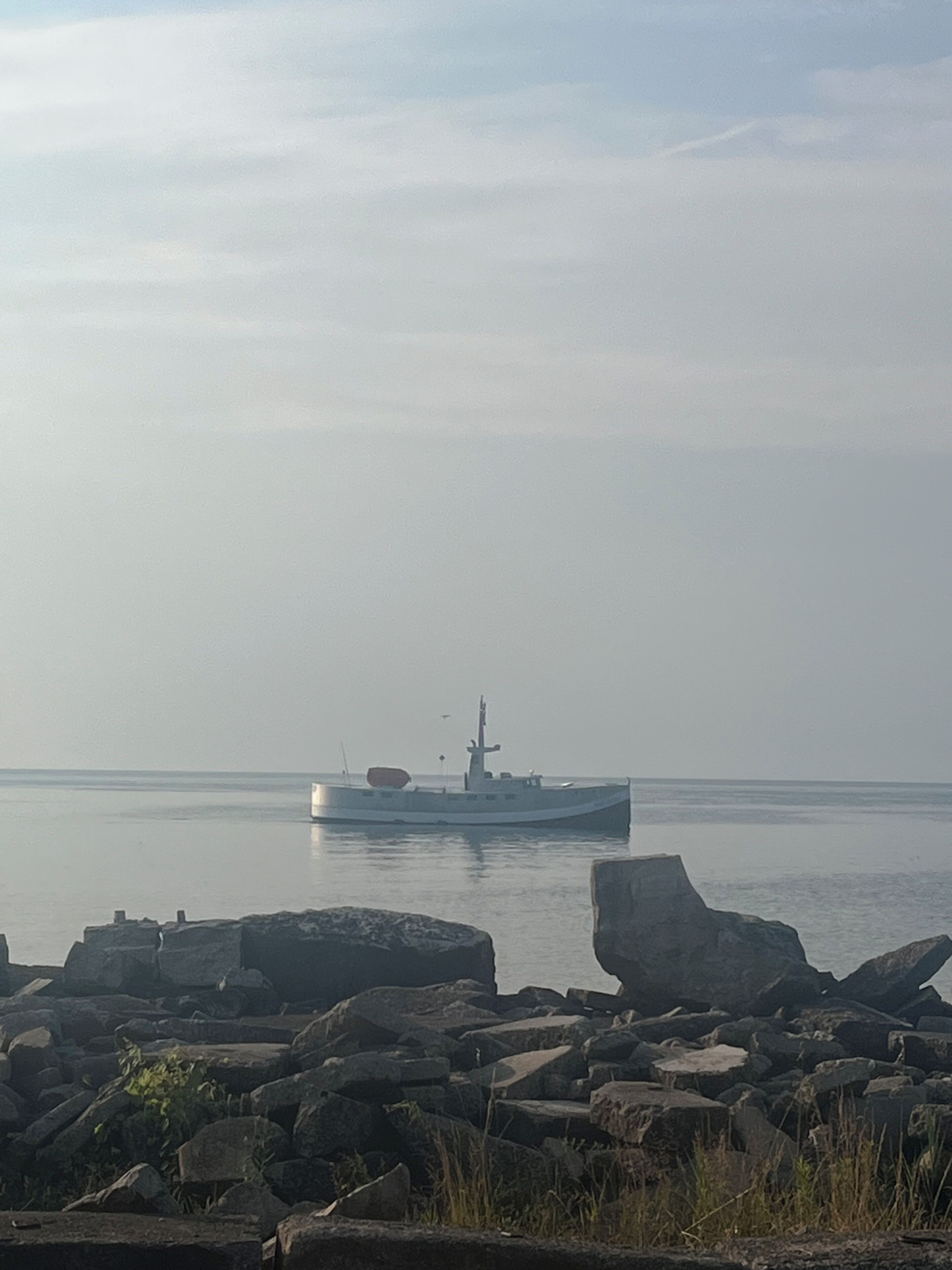 Un bateau sur une étendue d’eau calme, avec une côte rocheuse au premier plan.