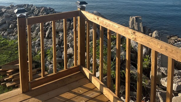 Una terraza de madera con barandilla que da a un mar tranquilo y un litoral rocoso.