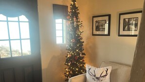 Una sala de estar con un árbol de Navidad, un sofá con un cojín de ciervo y una mesa de centro blanca con una vela.
