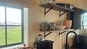 Una cocina con ventana, cafetera, estantes con frascos y un lavabo.