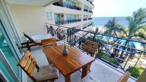 Un balcone con un tavolo e sedie di legno, affacciato su una piscina e palme.