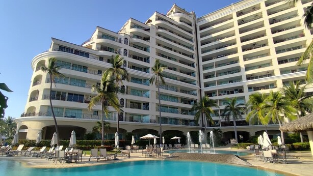 Un hotel con una piscina ampia, diversi balconi e palme.