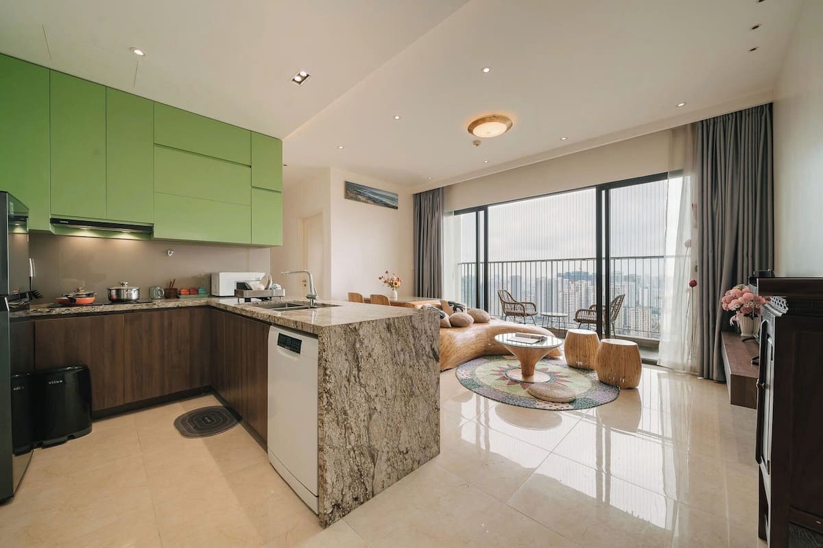 A modern kitchen with green cabinets, a marble island, and a dining area with a round table and chairs.