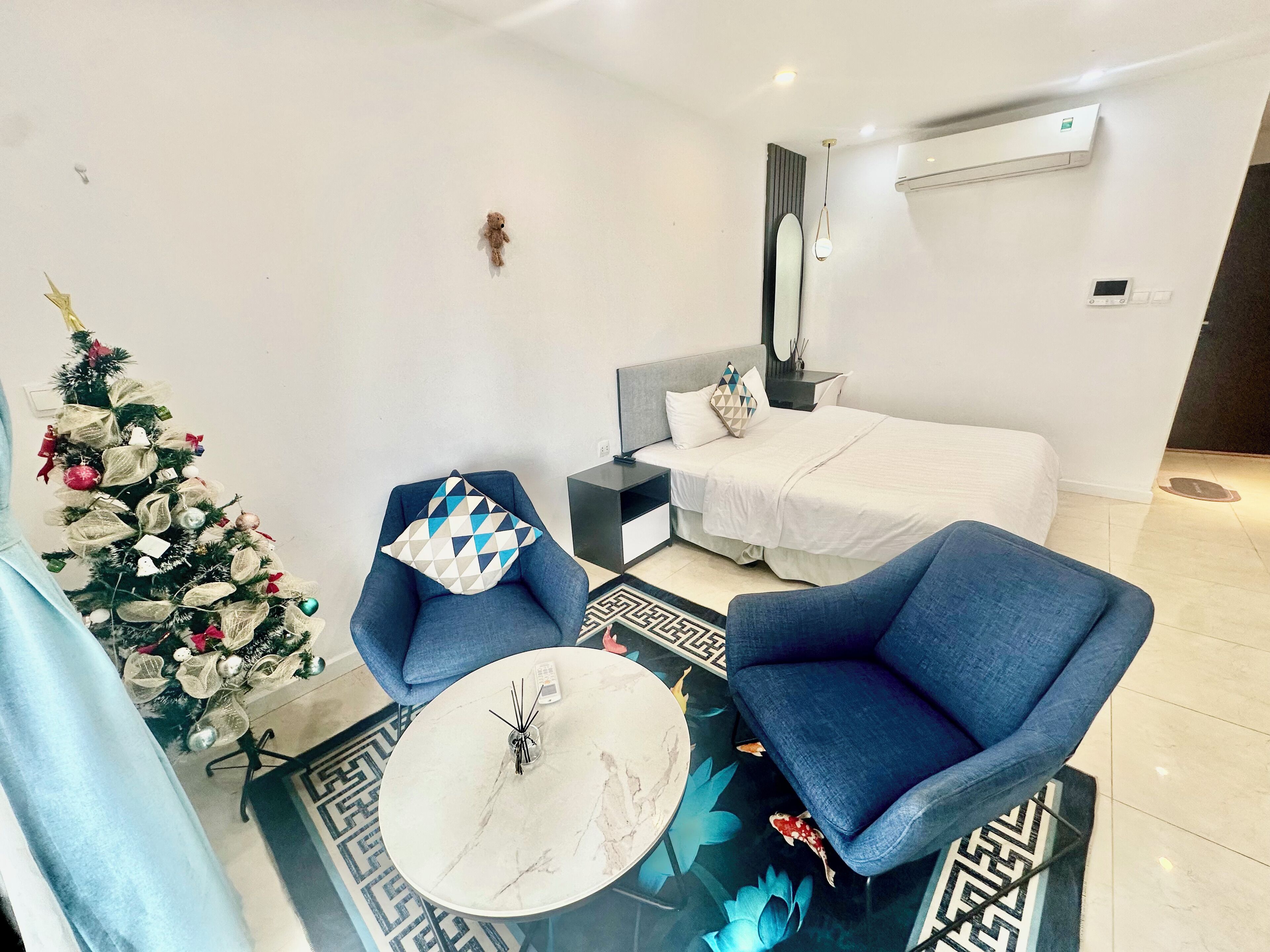 A modern hotel room with a bed, a desk, a chair, a coffee table, and a Christmas tree.