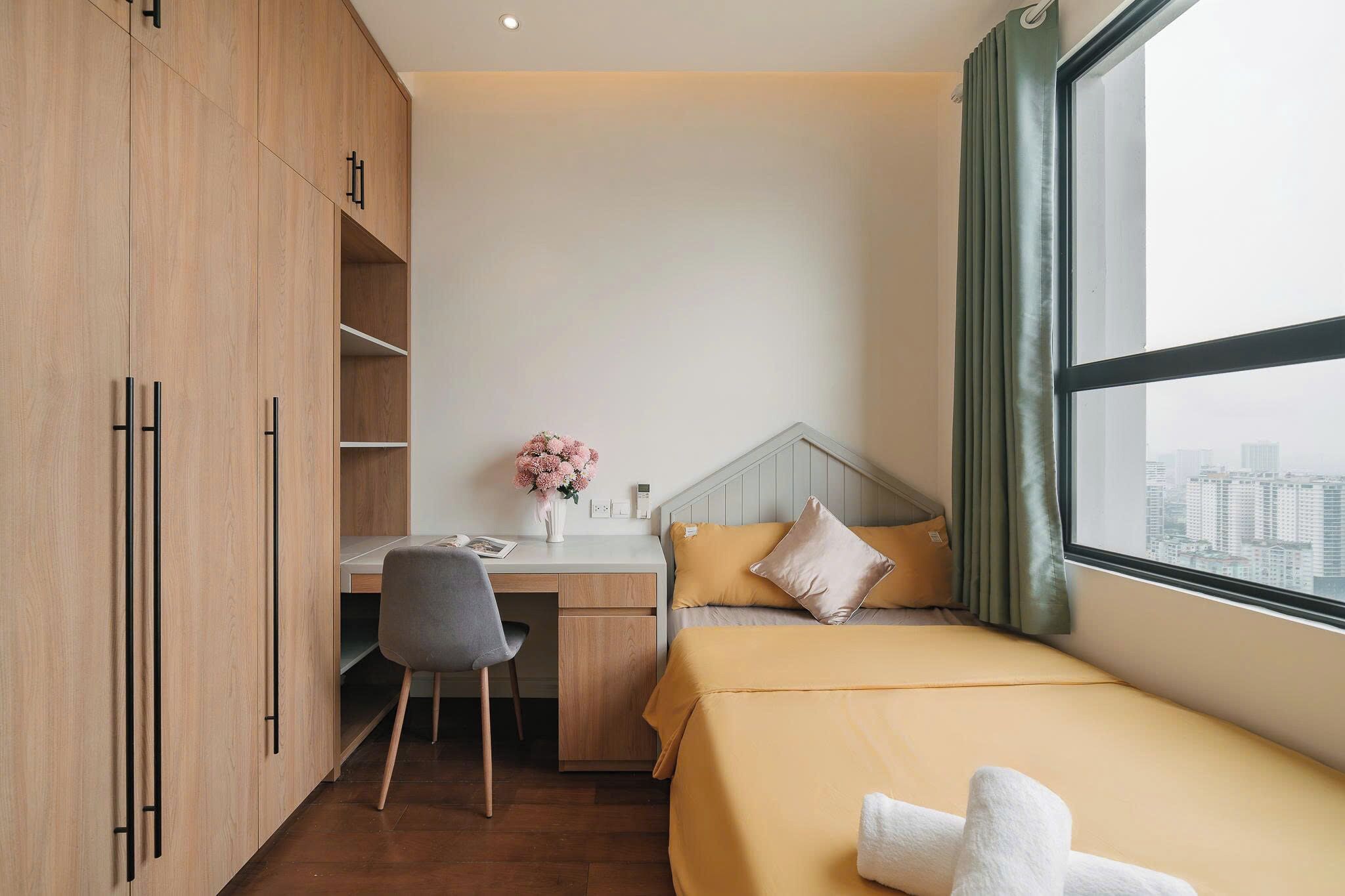 Une chambre d’hôtel avec un lit, un bureau et une chaise. Il y a une fenêtre avec des rideaux et une vue sur les bâtiments à l’extérieur.