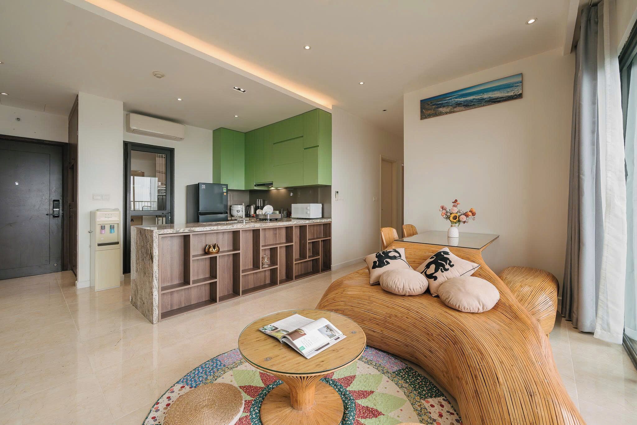 A modern hotel room with a kitchenette, a sofa with cushions, a small round table, and a view of the city.