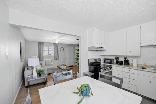 A modern kitchen with white cabinets, a dining area with a white table, and a living room with a sofa and a coffee table.