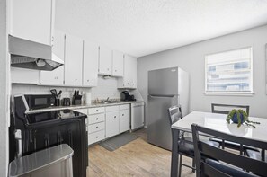 A modern kitchen with white cabinets, a black stove, and a stainless steel refrigerator.