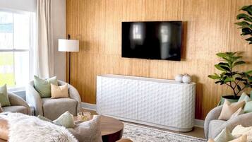Un salon moderne avec un ventilateur de plafond, un téléviseur à écran plat fixé sur un mur en bois, un meuble blanc et un tapis à motifs.