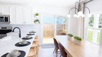Une cuisine moderne avec des meubles blancs, un îlot central doté de tabourets et un coin repas avec une longue table et des chaises en bois.