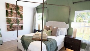 A four-poster bed with a wooden frame, a bedside table, a nightstand, and a wall-mounted plant. - North Boulevard Breeze Stylish New Home Near Beaches & Historic District (St. Augustine)