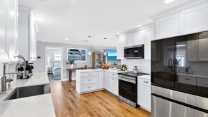 A modern kitchen with white cabinetry, stainless steel appliances, and wooden flooring. - Canalfront 3BR Heated Pool With Boat Lift (Punta Gorda)
