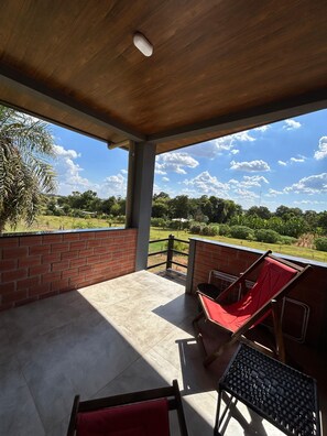 Un patio cubierto con dos sillas rojas acolchadas y una pequeña mesa, con vistas a un paisaje verde exuberante.