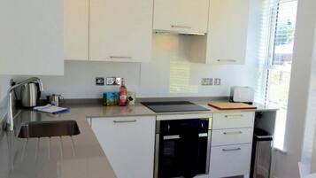 Une cuisine moderne avec des armoires blanches, des appareils en acier inoxydable et un parquet en bois disposé en chevrons.