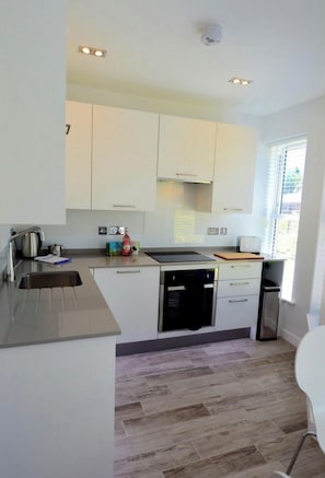 A modern kitchen with white cabinets, stainless steel appliances, and a herringbone wood floor.