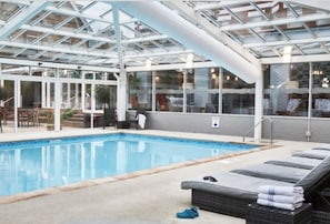 A swimming pool with lounge chairs and a glass-enclosed roof.